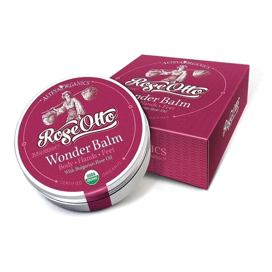 An organic tin of Wonder Balm Rose Otto Body-Hands-Feet Moisturizing, infused with Bulgarian Rose Otto, sitting in front of a box.