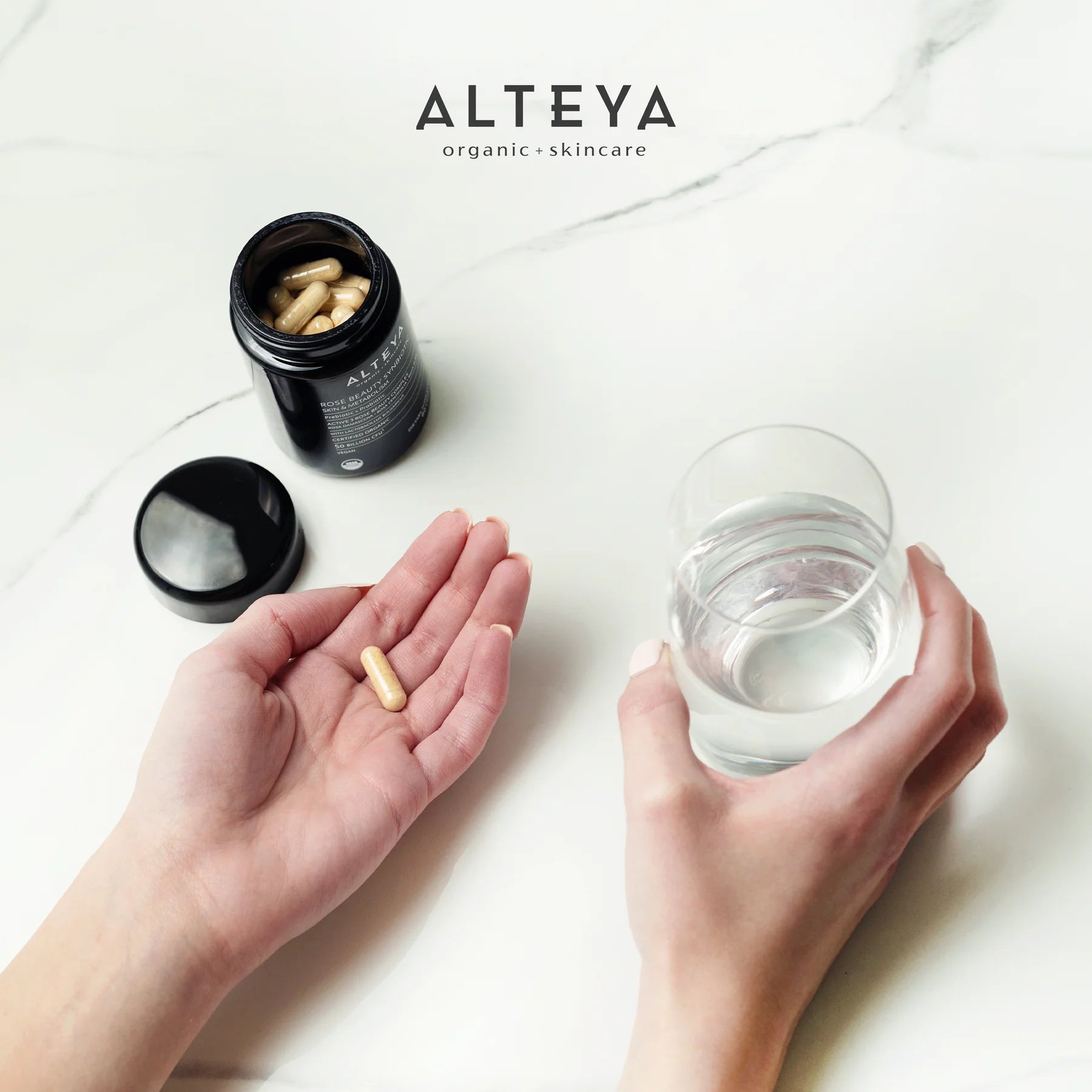 A hand holding a Rose Beauty Prebiotic and Probiotic - Synbiotic Skin & Metabolism Vegan Organic Supplement next to a bottle of pills for optimal gut health.