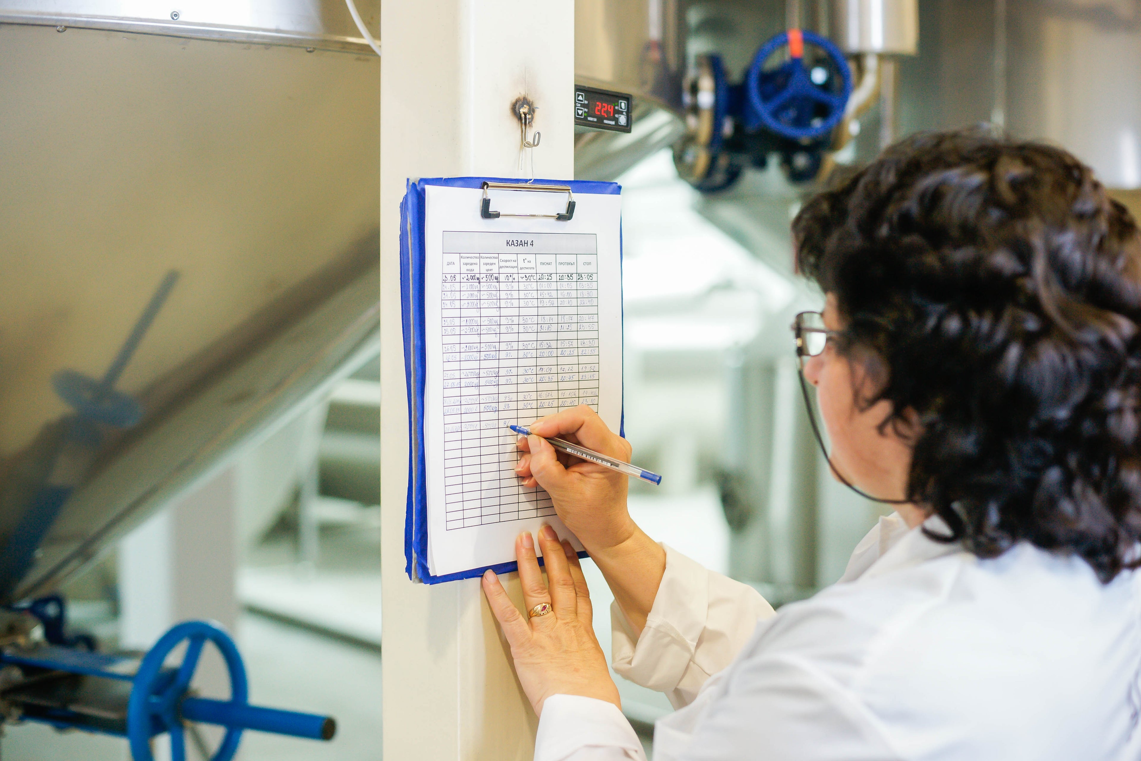 A woman in a lab coat with expertise in rosa damascena, carefully writing on a clipboard.