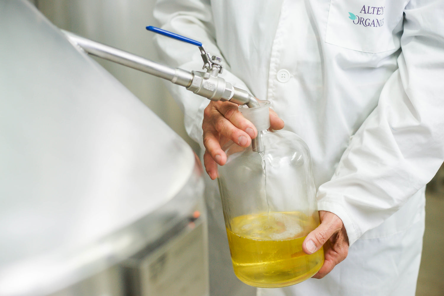 A person in a lab coat pouring Bulgarian rose liquid into a container.