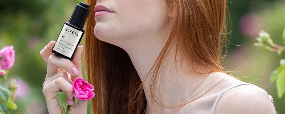 A woman with red hair is smelling a rose from the bulgarian rose fields.