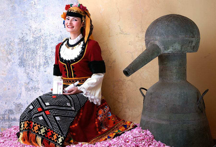 A woman in a traditional dress sits on a pink wall amidst rosa damascena and rose fields.