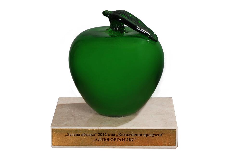 A green glass apple on a pedestal surrounded by rose fields.