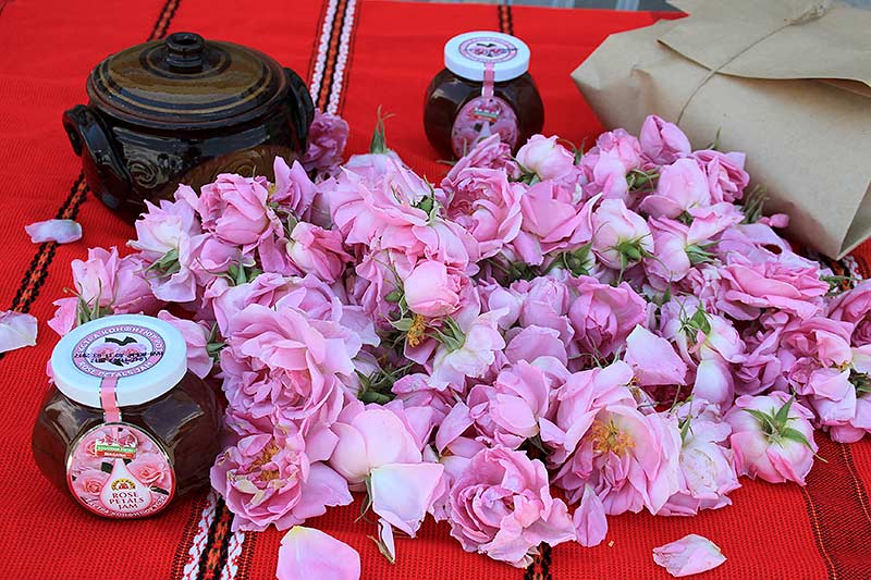 A table with a jar of honey surrounded by pink roses.