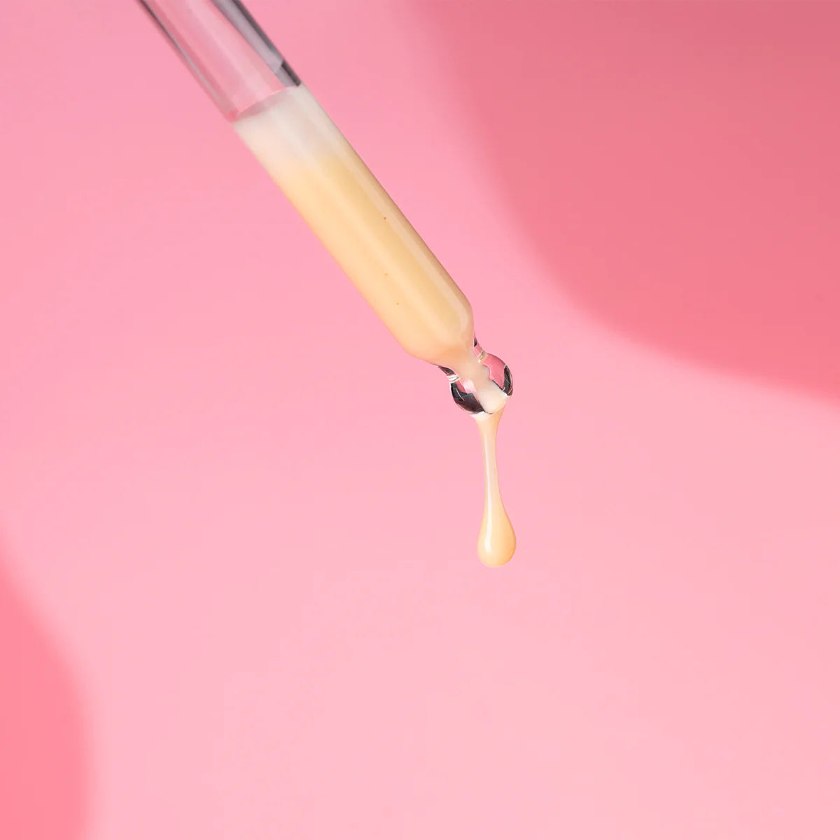 A person is pouring Bio Damascena Regenerating Concentrate into a tube on a pink background.