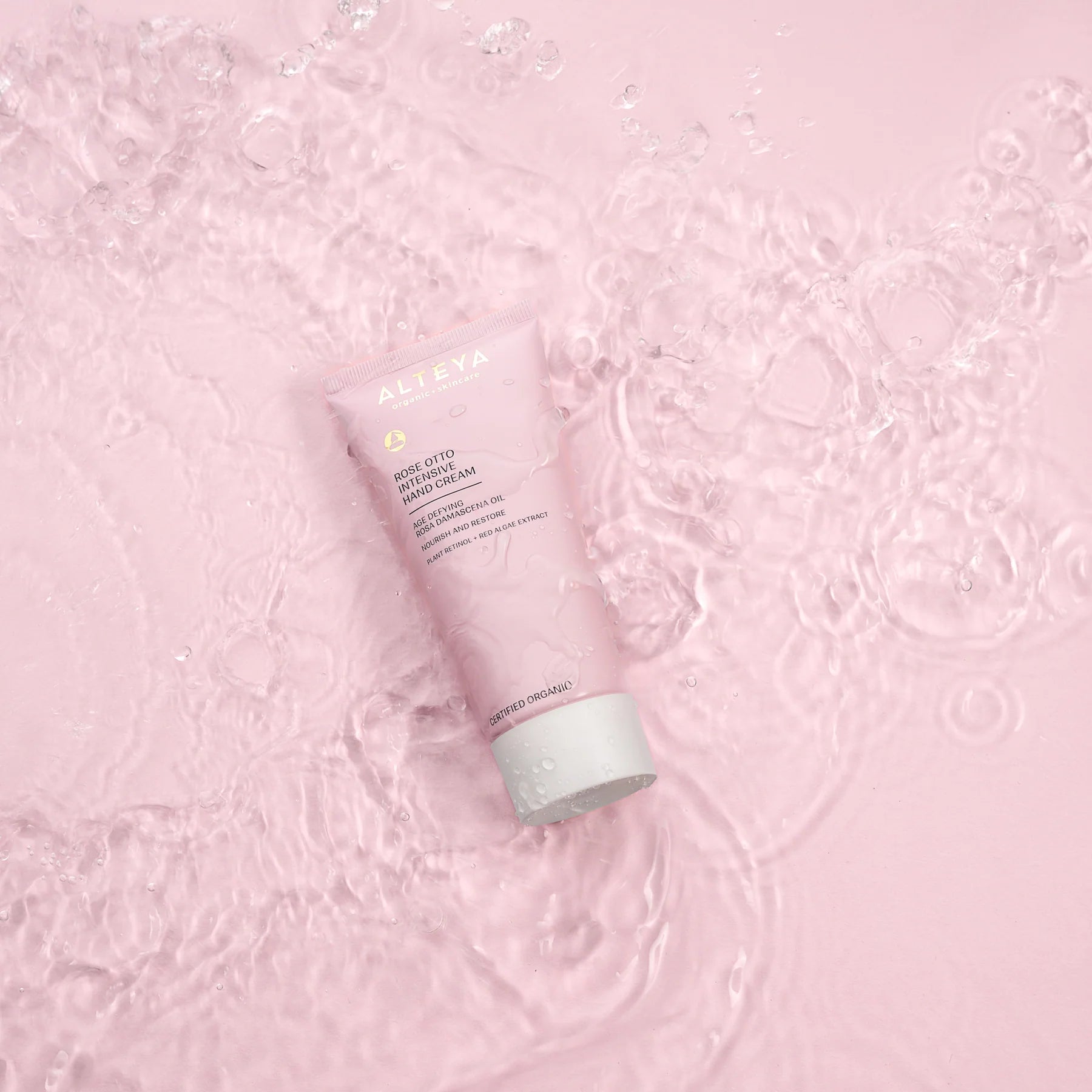 A tube of Organic Rose Otto Intensive Hand Cream on a pink background.