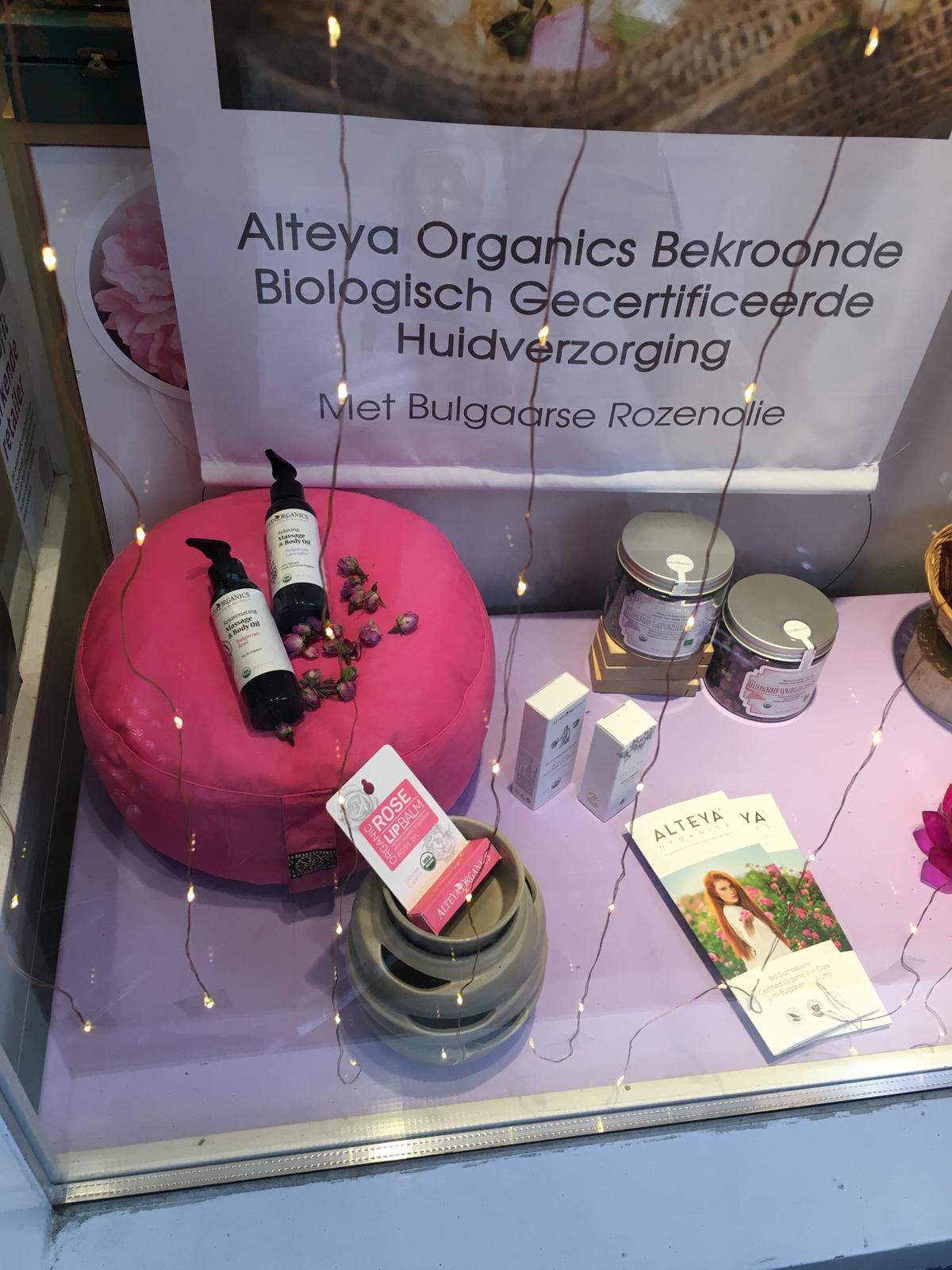 A window display featuring a pink pillow adorned with rose petals and other items.