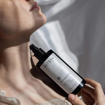 A woman holding a bottle of Rose Otto Facial Toner Bio Damascena, as part of her skincare routine.