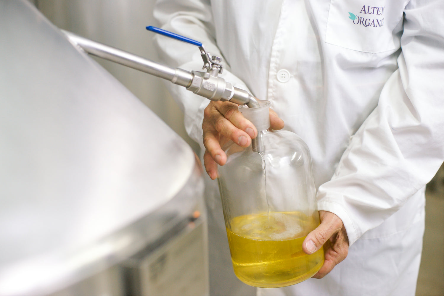 A person in a lab coat pouring rosa damascena liquid into a container.