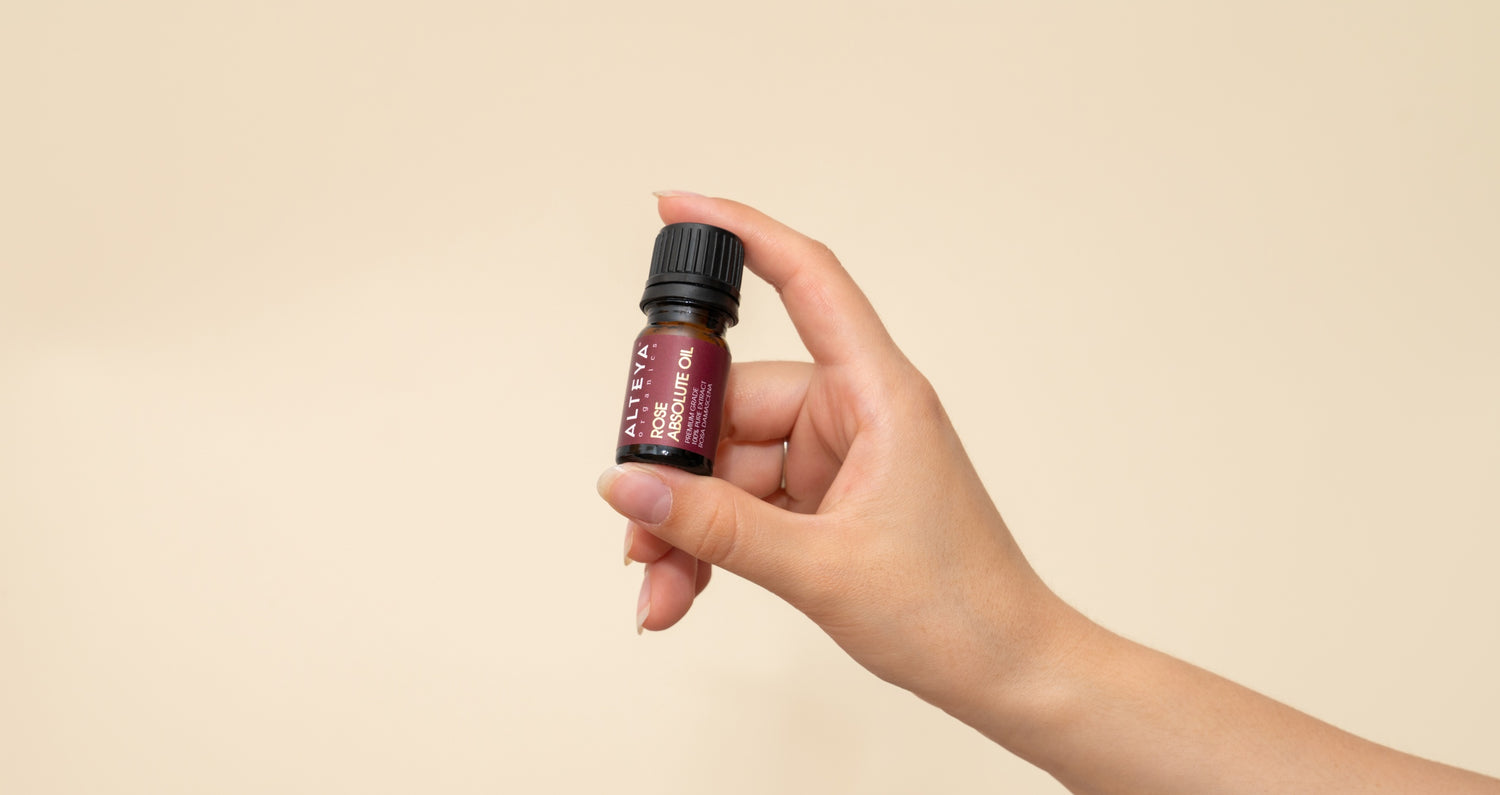 A hand holding a small bottle of luxurious, fragrant Rose Absolute Oil - 100% Pure essential oil.