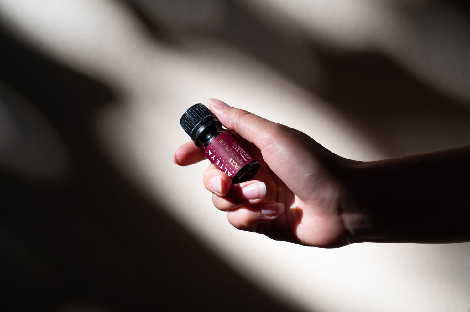 A person's hand holding a bottle of Bulgarian rose essential oil.