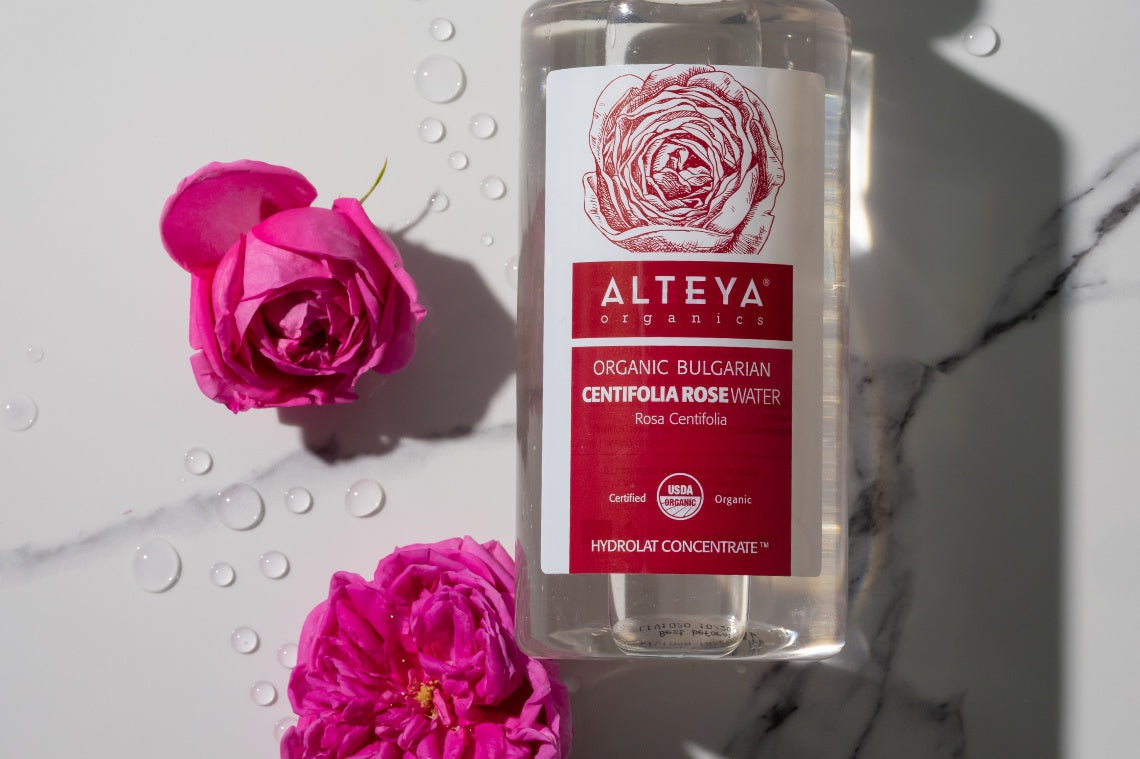 A bottle of alteya organic toner next to a pink rose in a field of rose fields.