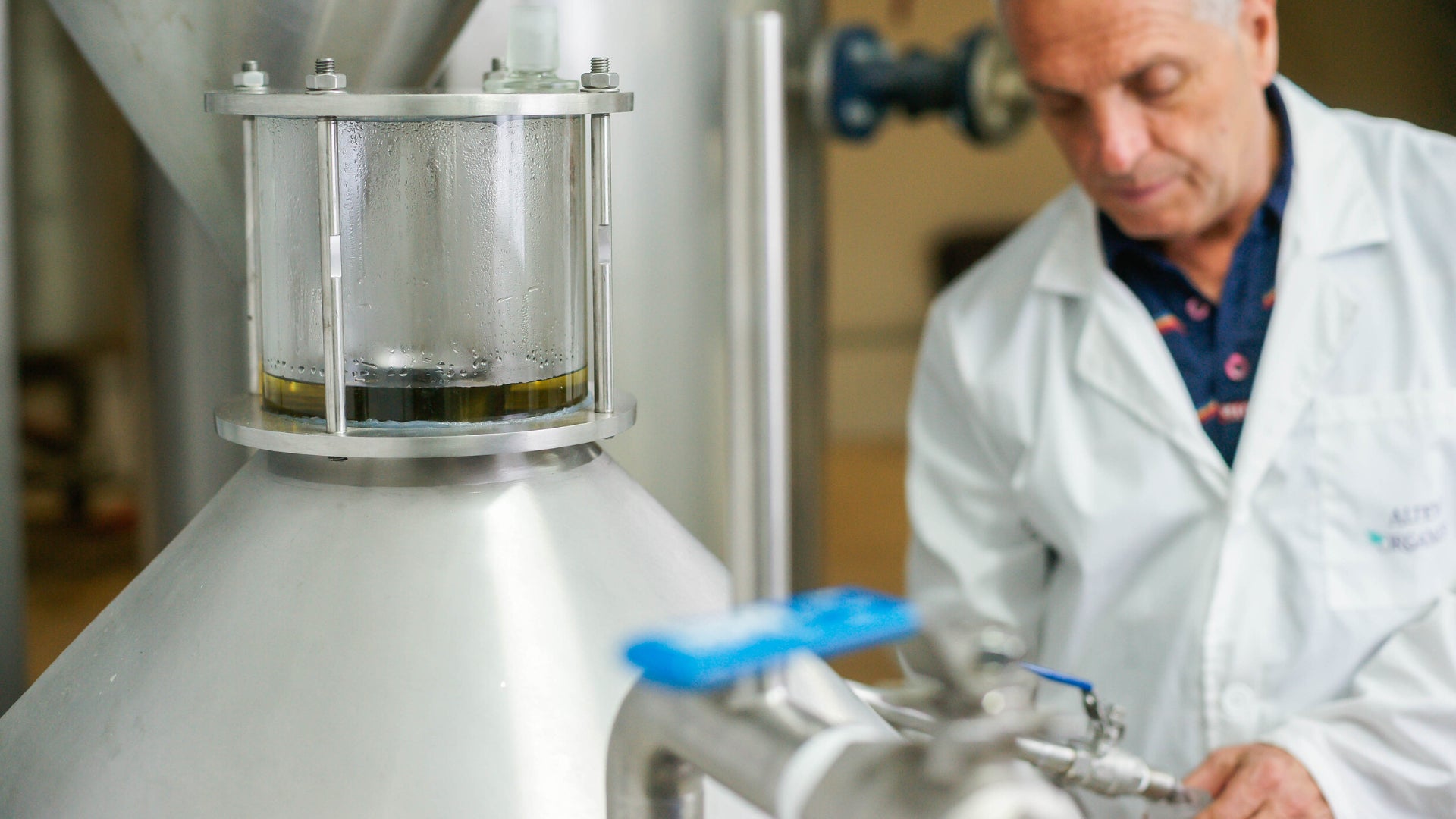 A man in a lab coat is pouring Bulgarian rose oil into a tank.